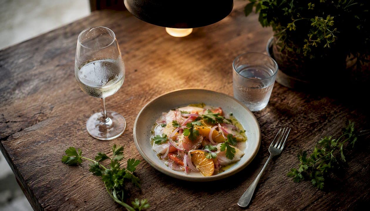 Un gin délicatement servi en accompagnement d’un ceviche, le tout présenté sur une table en bois brut.
