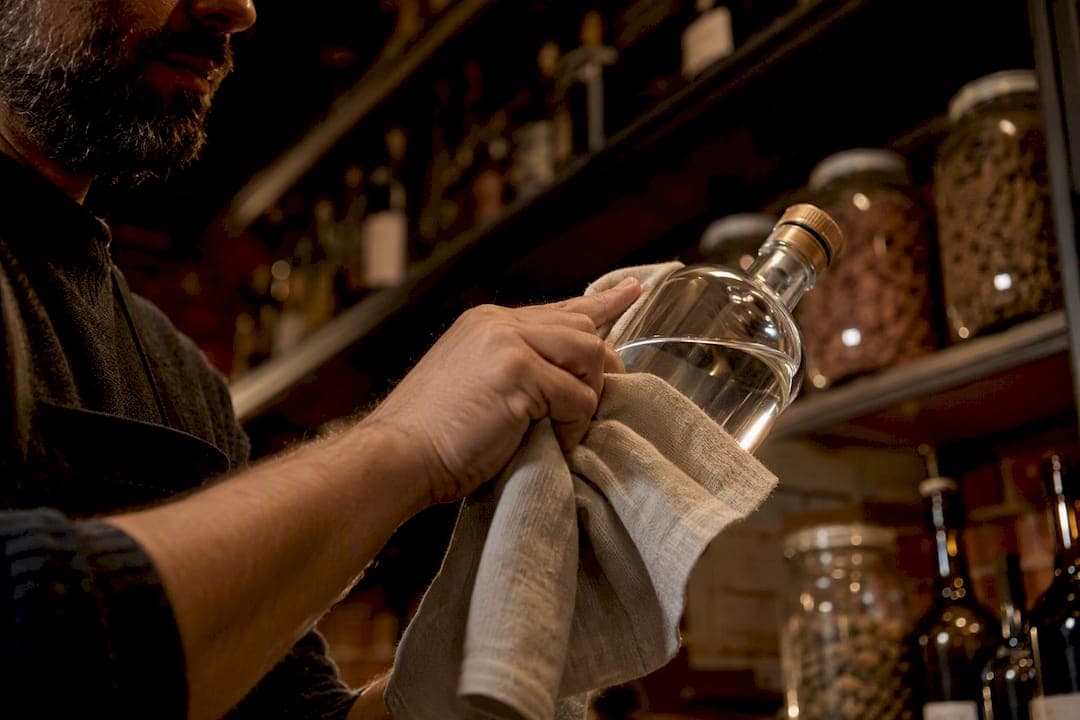 Personne essuyant le goulot d'une bouteille de gin avec un chiffon