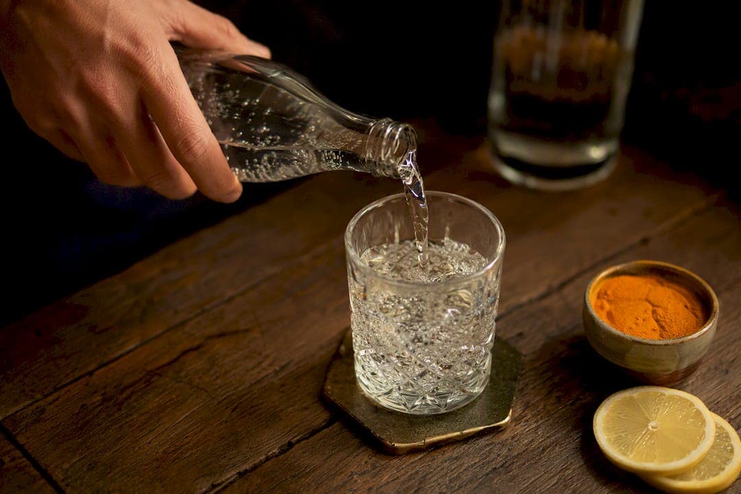 Main versant de l'eau pétillante dans un verre artisanal à spritz